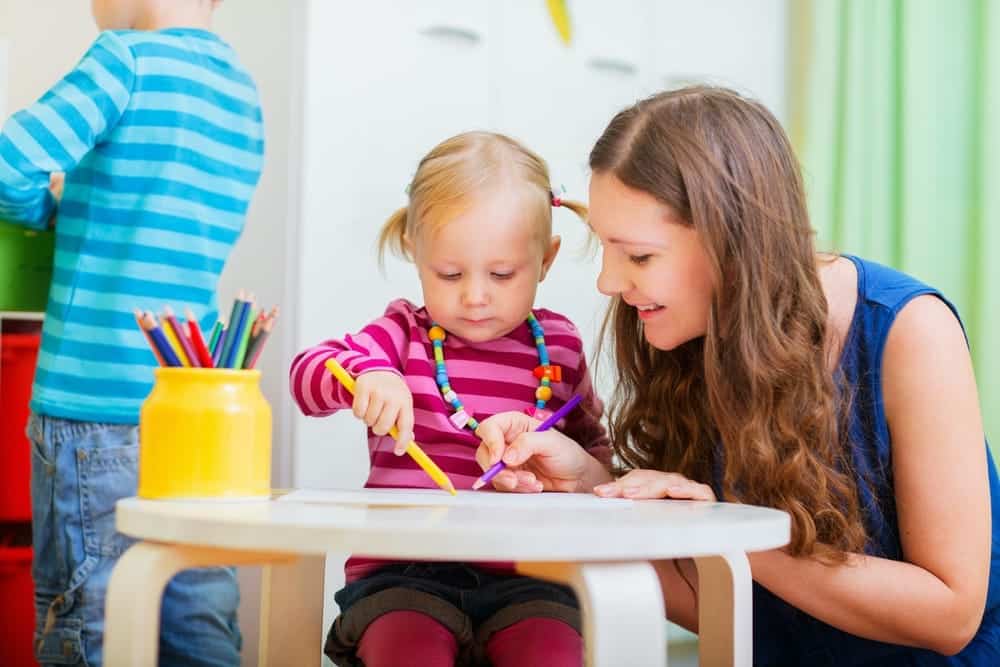 une assistante maternelle accompagne une petite fille dans son atelier de coloriage